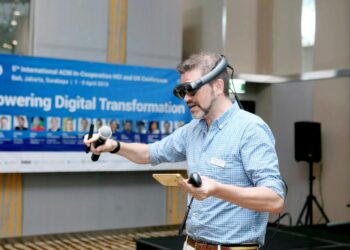 Pria dengan kemeja kancing kotak-kotak biru dan putih memegang mikrofon berkabel hitam dan coklat